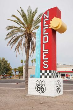 there is a large sign on the side of the road in front of a palm tree