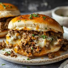 two cheeseburger sandwiches on a plate with sauce and green garnishes