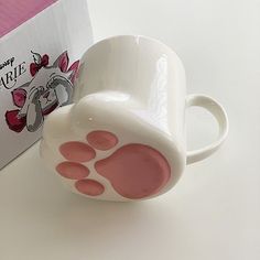 a coffee cup with pink paw prints on it next to a disney mouse mug and box