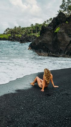 a woman is laying on the black sand by the water's edge, with her back turned to the camera