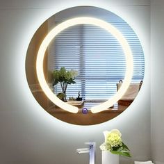 a bathroom sink with a round mirror on the wall above it and flowers in a vase