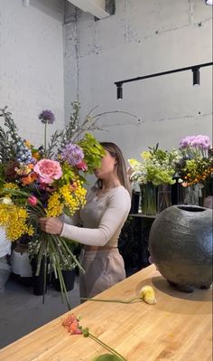 a woman arranging flowers on a table in a room with large vases and tables