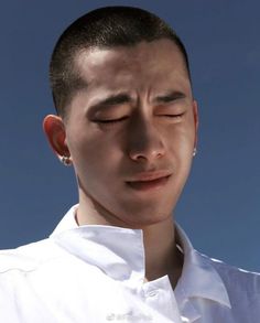 a young man with his eyes closed looking down at something in the sky behind him