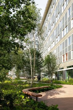 the building has many windows and trees in front of it, along with a bench