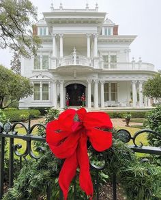 a large white house with a red bow on it's front gate and bushes