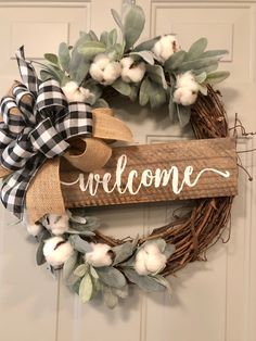 a welcome sign hanging on the front door with cotton flowers and greenery around it