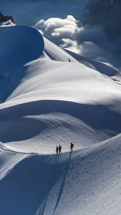 two people walking up the side of a snow covered mountain with clouds in the background