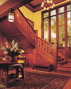 a room with wooden stairs and chandelier in the center, next to a table with flowers on it