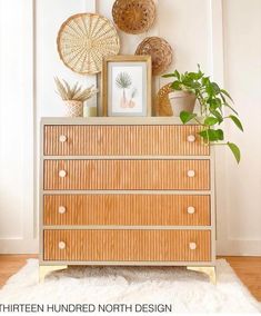 a wooden dresser sitting in front of a white wall with pictures and plants on it