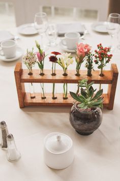 there are many flowers in the vases on this wooden rack at the head table