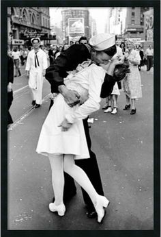 a man and woman kissing in the middle of a city street with people walking around