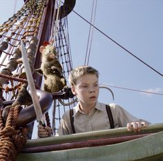 a young boy standing on top of a boat next to a monkey sitting on the mast