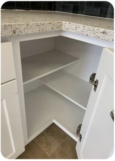 an open cabinet in a kitchen with marble counter tops