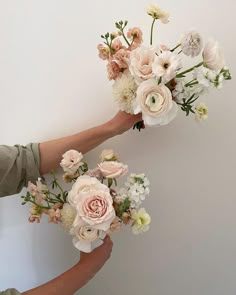 two hands holding flowers against a white wall