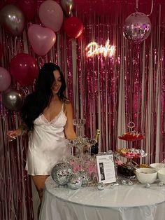 a woman standing in front of a table filled with food and drinks, surrounded by balloons