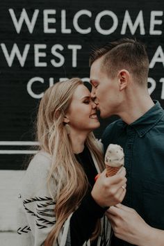 a man and woman kissing while holding an ice cream cone in front of a welcome sign