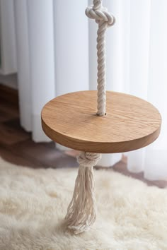 a round wooden table with rope on top and white rug in front of the window