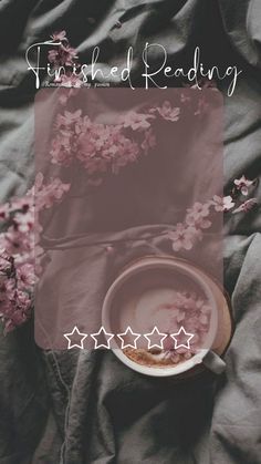 a coffee cup and saucer sitting on top of a bed next to pink flowers