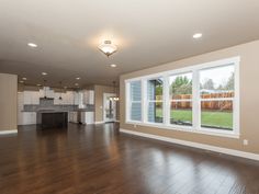 an empty living room with hard wood flooring and large open windows overlooking the backyard