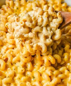 macaroni and cheese being stirred with a wooden spoon