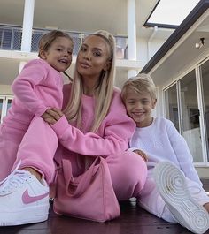 a woman and two children sitting on the ground in front of a house with their arms around each other