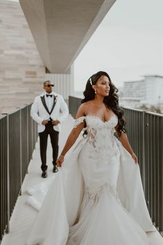 a woman in a wedding dress walking down a walkway next to a man in a tuxedo