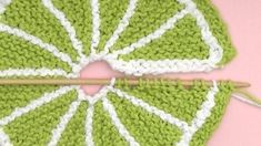 a green and white crocheted umbrella sitting on top of a pink table next to a knitting needle