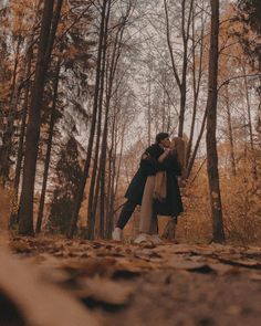 a man and woman kissing in the woods surrounded by autumn leaves, with trees behind them