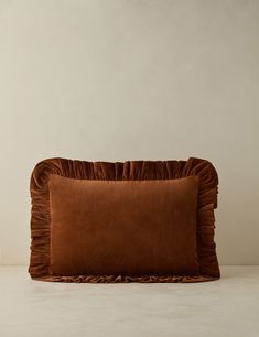 a brown pillow with ruffled edges on a white table next to a candle holder