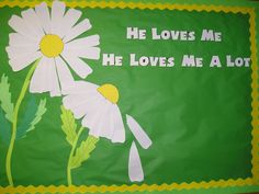 a green banner with white daisies and the words he loves me he loves me a lot