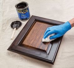 a person in blue gloves is cleaning a wooden frame with a rag and paintbrush