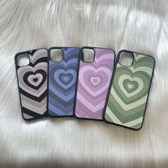 four iphone cases with hearts on them sitting on a white sheet, one has a heart in the middle