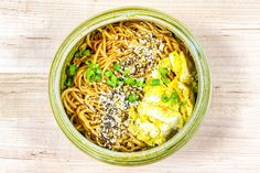 an overhead view of a bowl of noodles with eggs and chives in it on a wooden table