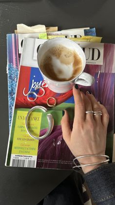 a person is reading a magazine with a cup of coffee on it and their fingers resting on the cover