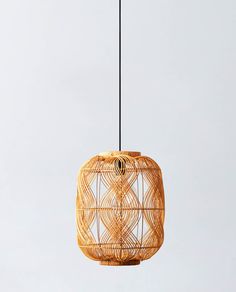 a rattan light fixture hanging from a wire on a gray background with a black cord