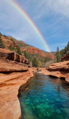 a rainbow shines in the sky above a river with clear blue water surrounded by red rocks