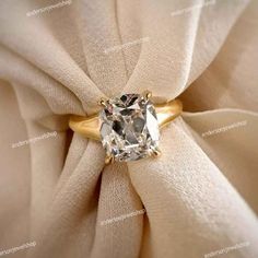 an engagement ring with a cushion cut diamond in the center on top of a white cloth