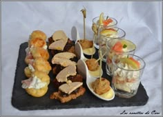 an assortment of appetizers are displayed on a black slate platter with spoons