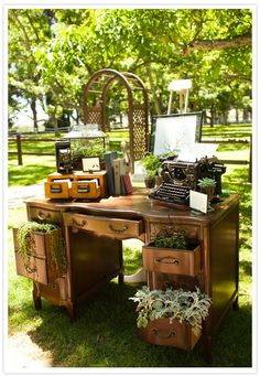 an old - fashioned desk is decorated with plants, books and vintage typewriters