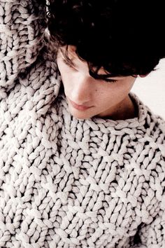 a woman wearing a knitted sweater is looking at her cell phone while she covers her face