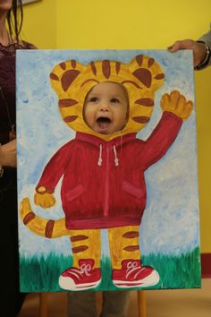 a child holding up a painting of a tiger wearing a red jacket and orange shoes