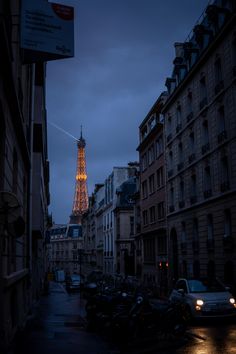 the eiffel tower is lit up at night in paris, france as seen from an alleyway