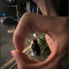 a person sitting on the ground with their fingers in the shape of a heart, looking up into the sky