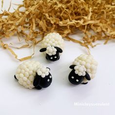 three sheep made out of beads sitting on top of some shredded paper next to it