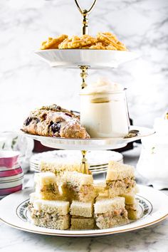 three tiered trays filled with food on top of a marble countertop next to cups and saucers