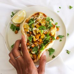 a person holding a piece of food on a white plate next to a lemon wedge