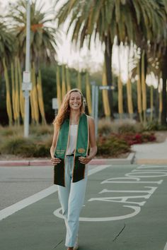 a woman is walking down the street wearing a green vest and white pants with palm trees in the background