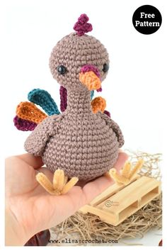 a small crocheted turkey sitting on top of a pile of hay next to a hand