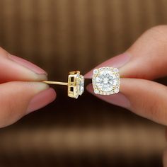 a pair of diamond stud earrings being held by someone's hand