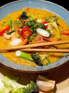 a bowl filled with soup and chopsticks next to broccoli